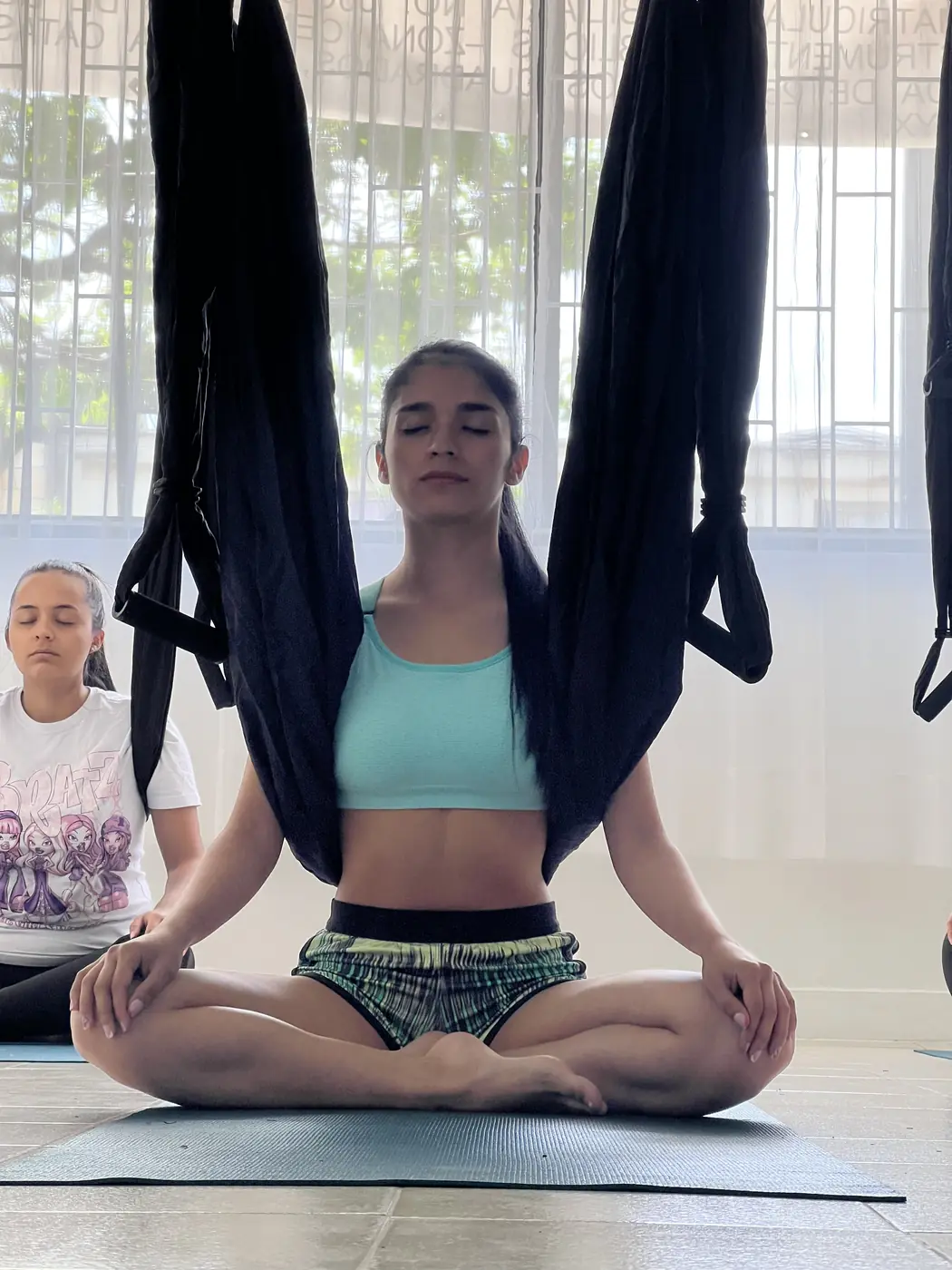 Alumna meditando con los ojos cerrados, sentada entre las telas del columpio